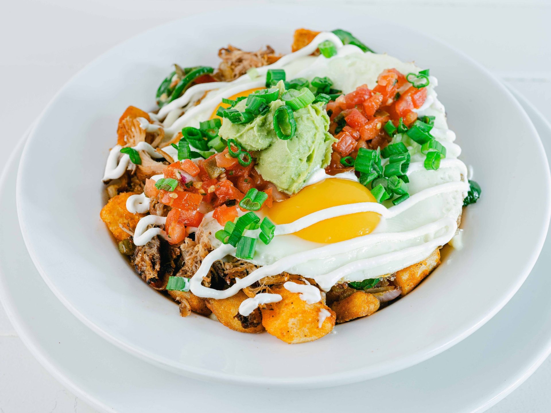 Carnitas hash bowl with two eggs, guacamole, pico and crema